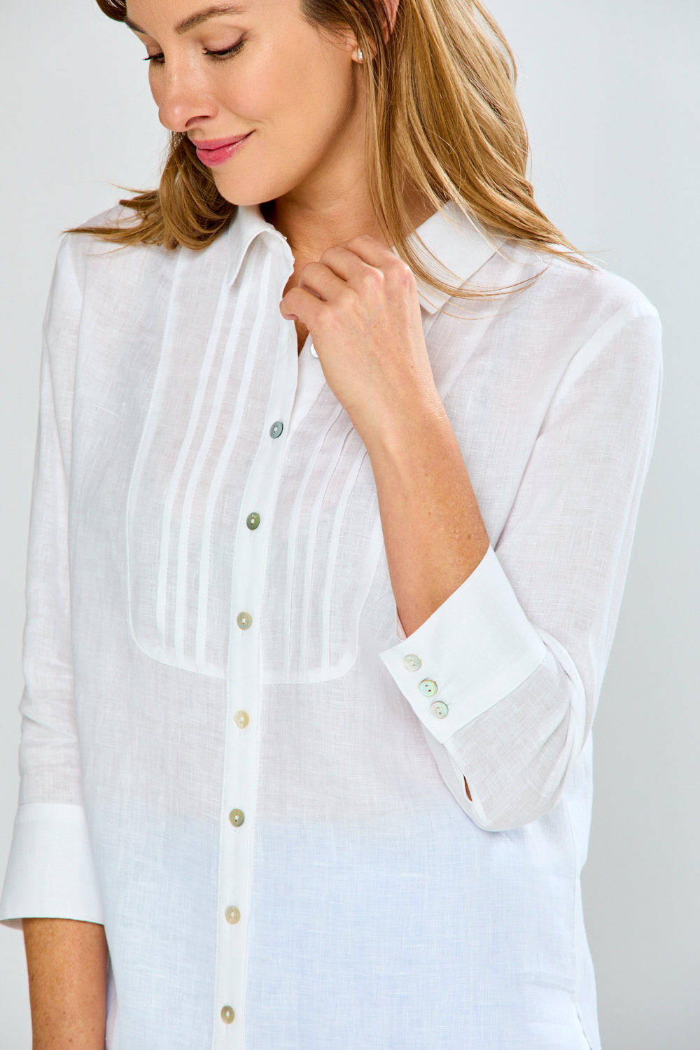 Woman wearing a white blouse with a subtle pattern on a plain background