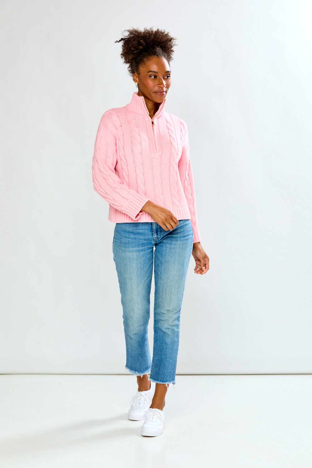 Person wearing a pink sweater and blue jeans against a white background