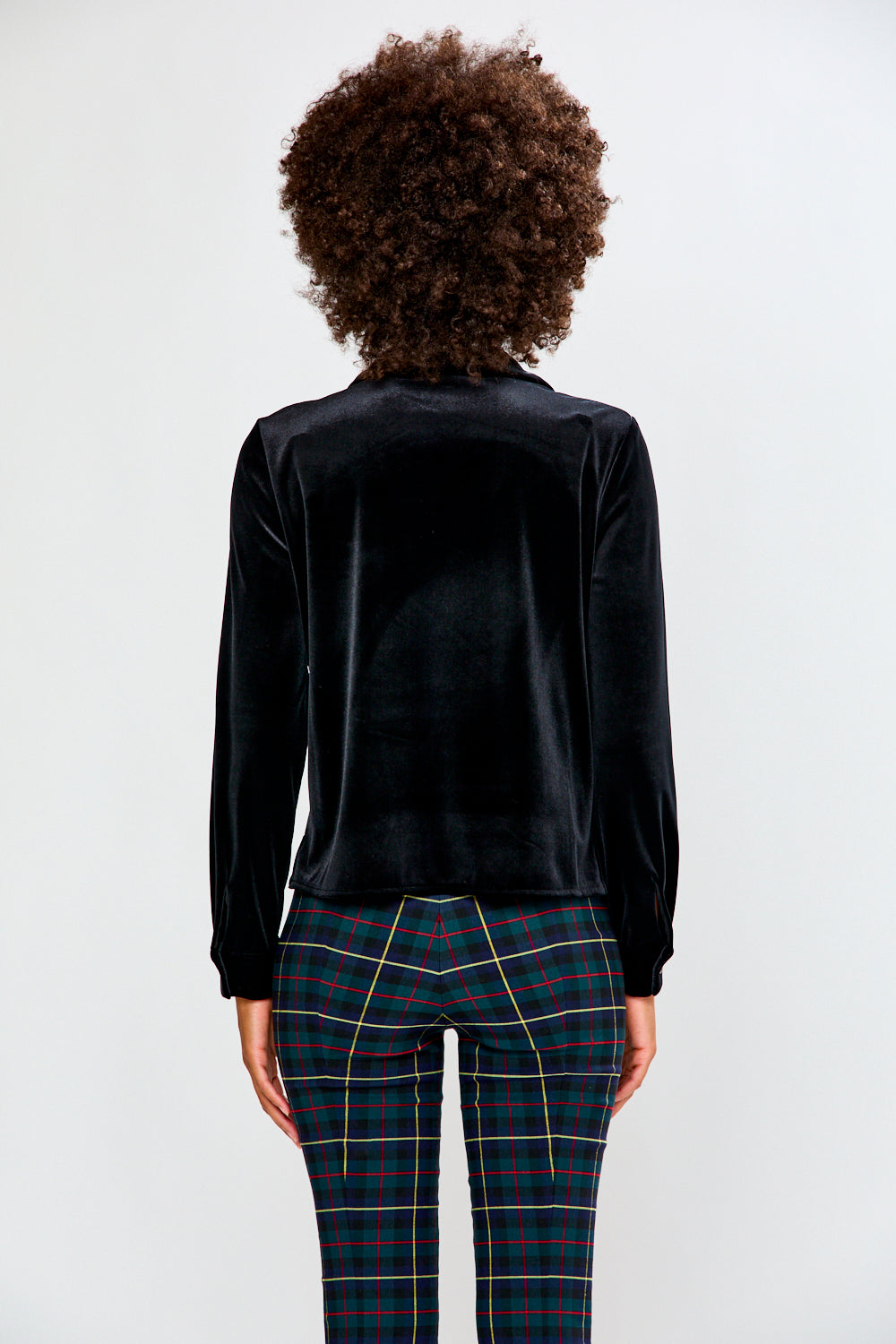Person wearing a black velvet shirt and plaid pants on a white background