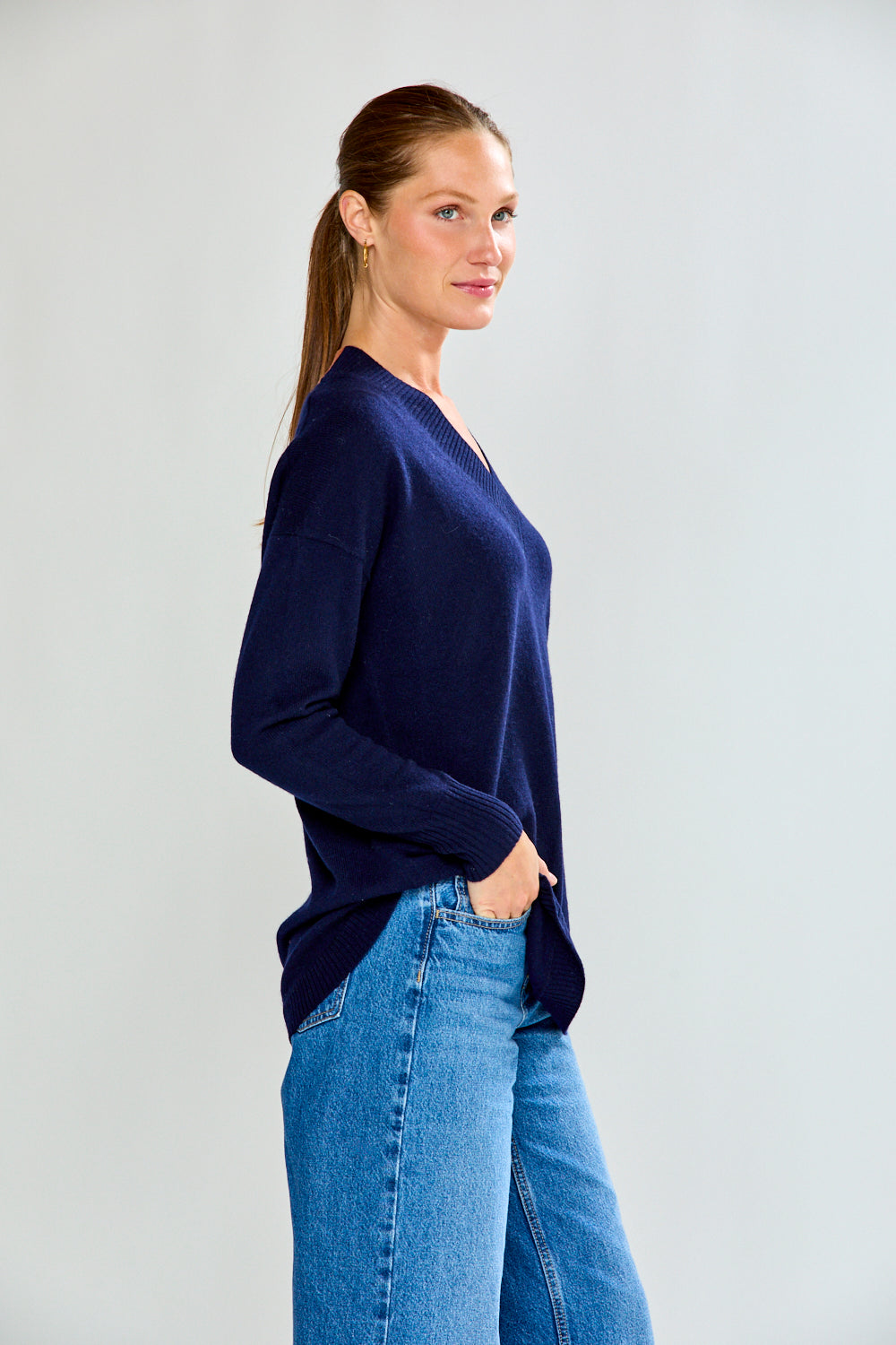 Woman wearing a navy sweater and blue jeans against a plain background