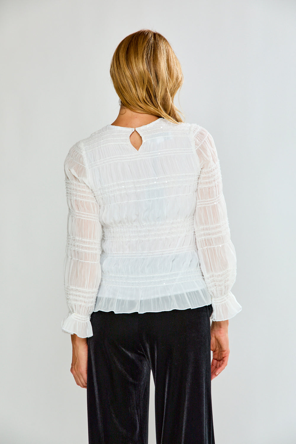 Person wearing a white blouse with long sleeves and black pants on a plain background