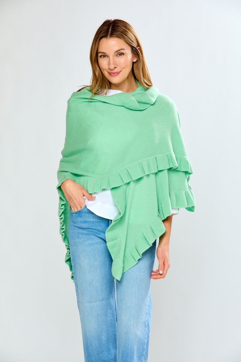 Woman wearing a light green poncho over a white top and blue jeans on a white background