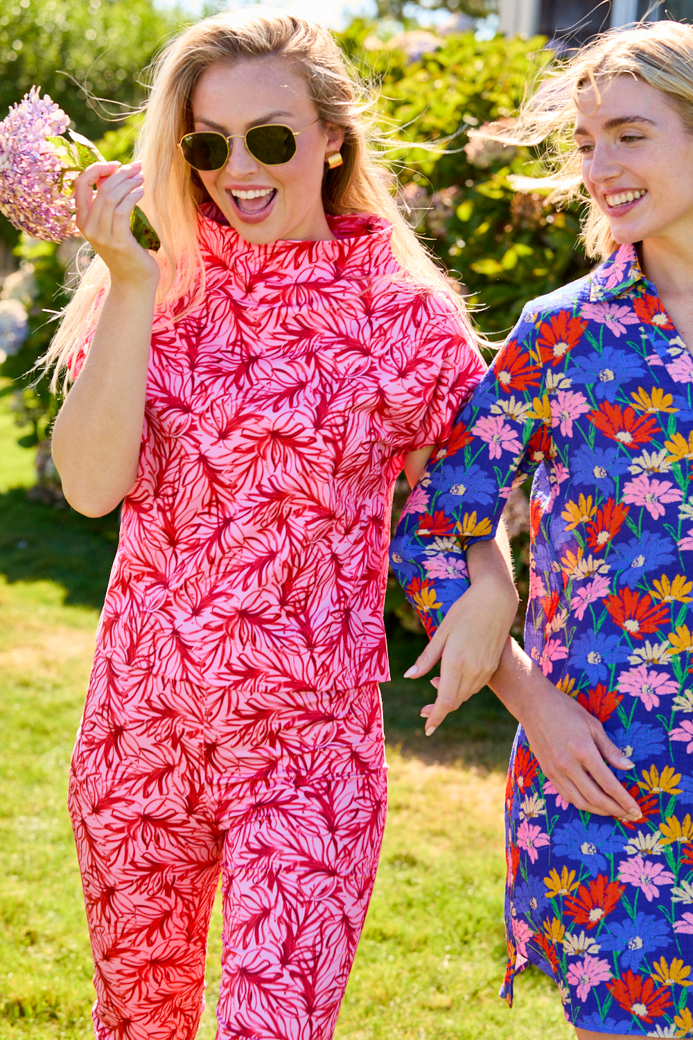 Two women in colorful outfits standing outdoors with greenery in the background