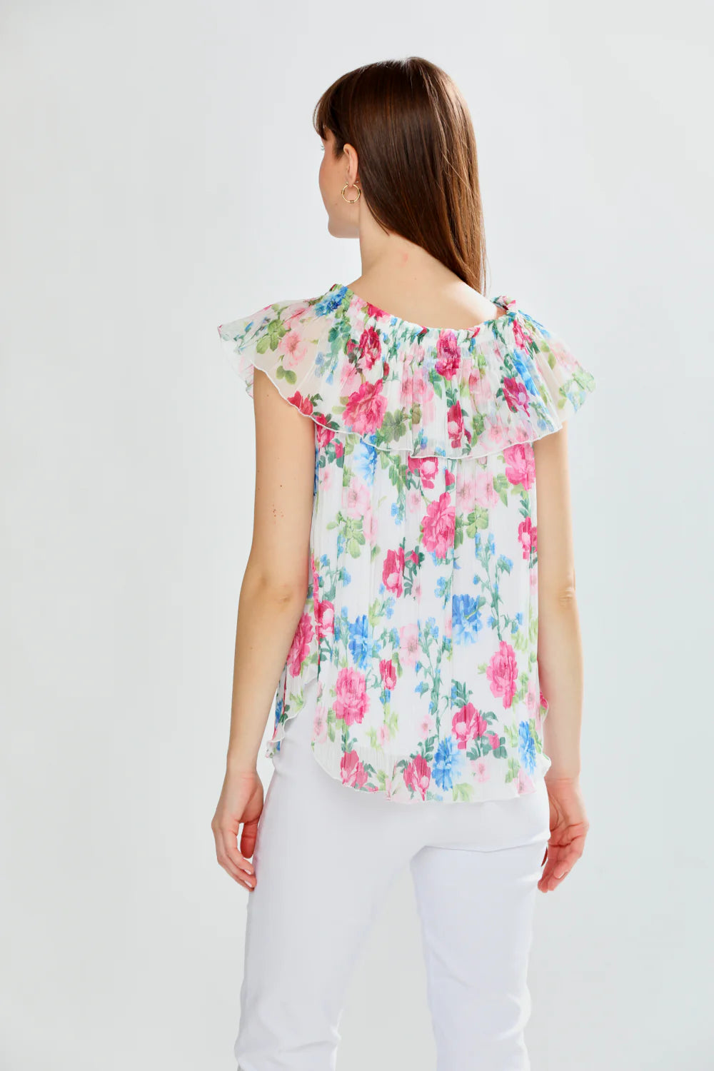 Woman wearing a floral blouse with white pants on a light gray background