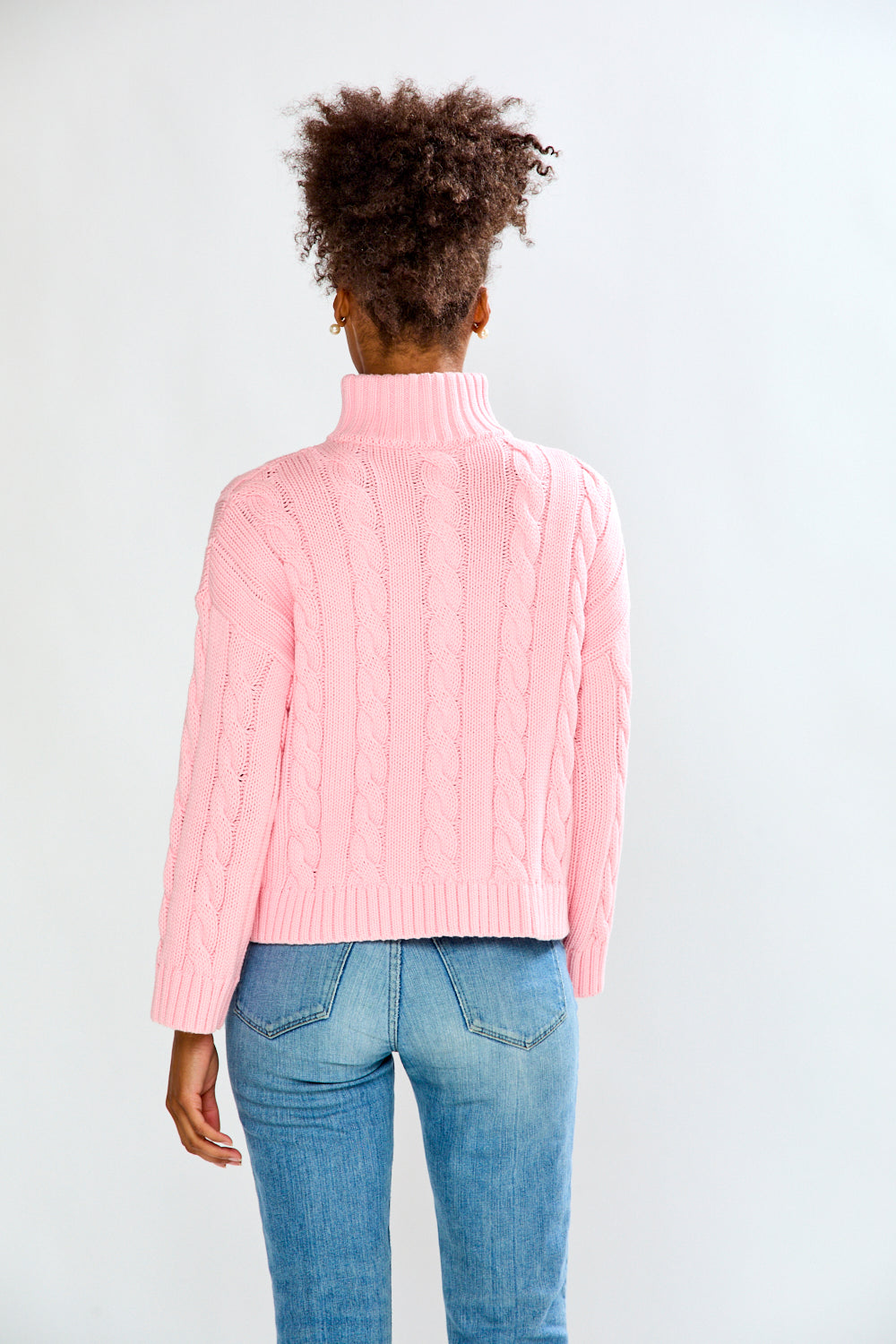 Person wearing a pink cable knit sweater and blue jeans on a white background