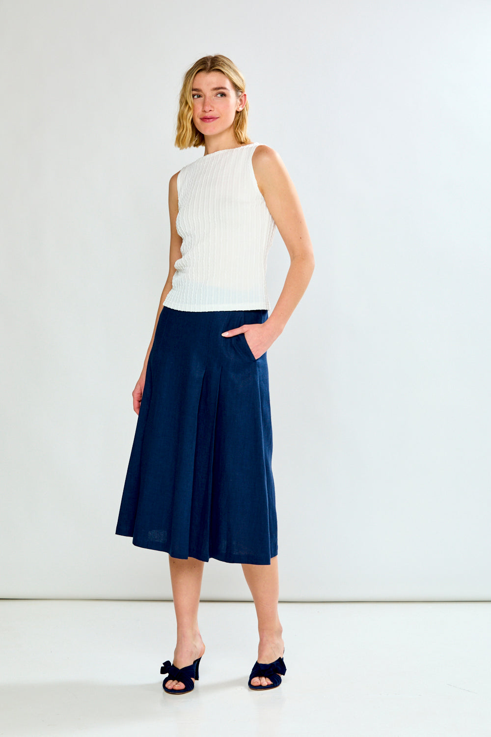 Woman wearing a white sleeveless top and navy skirt on a white background