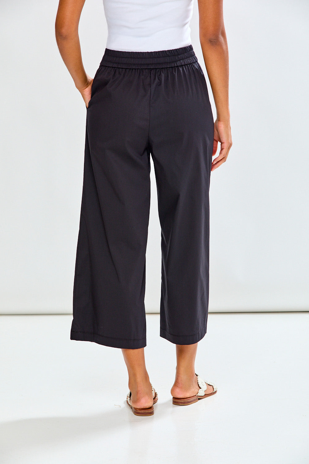 Woman wearing black wide-leg pants and white sandals on a white background