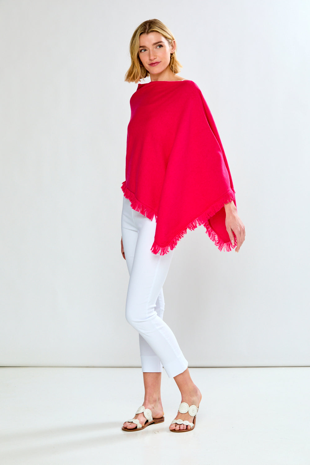 Woman wearing a bright pink poncho over a white top and pants on a white background