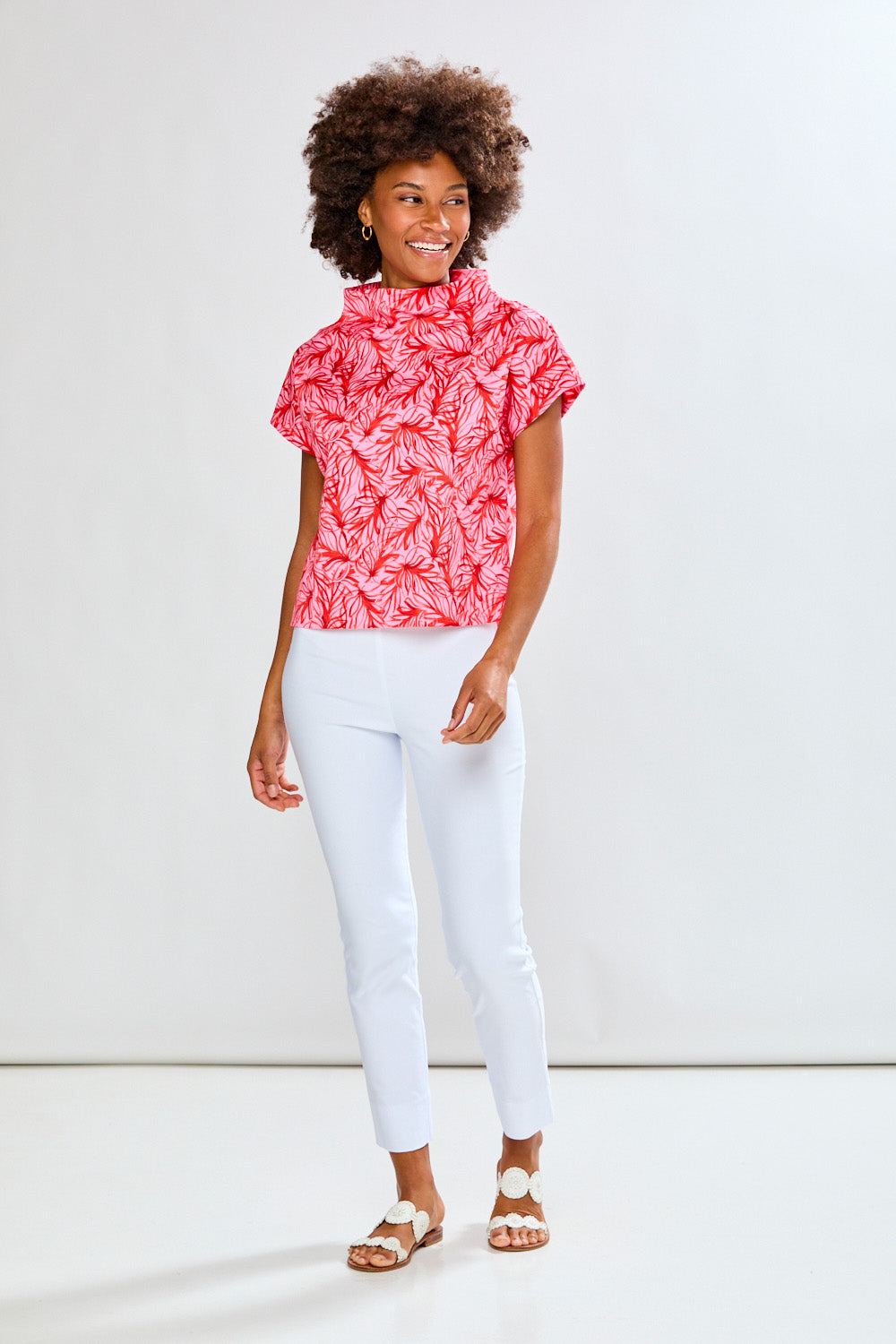 Woman wearing a pink patterned top and white pants on a white background