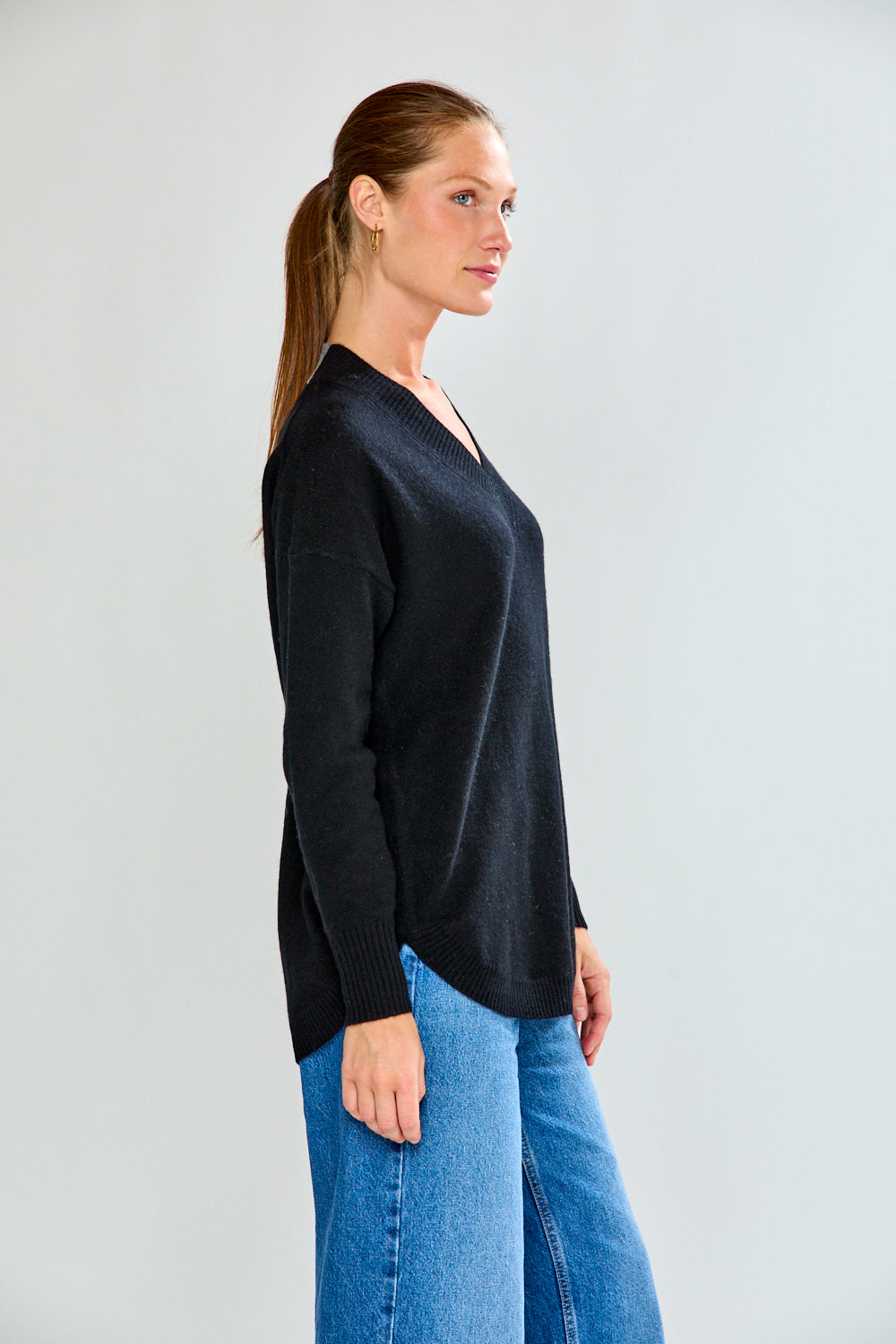 Woman wearing a black sweater and blue jeans against a plain background