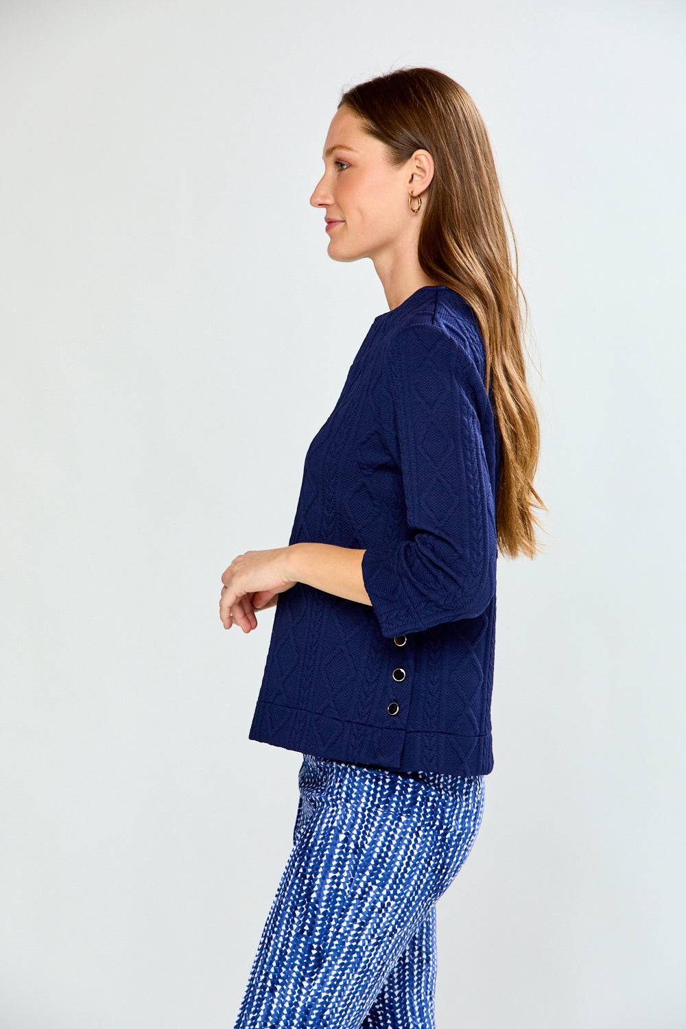 Woman wearing a navy blue cable knit top and patterned pants on a white background