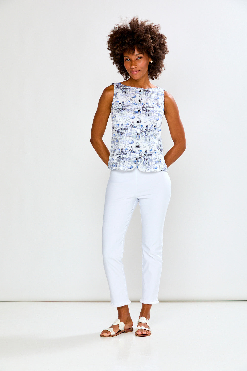 Woman wearing a patterned top and white pants against a plain background
