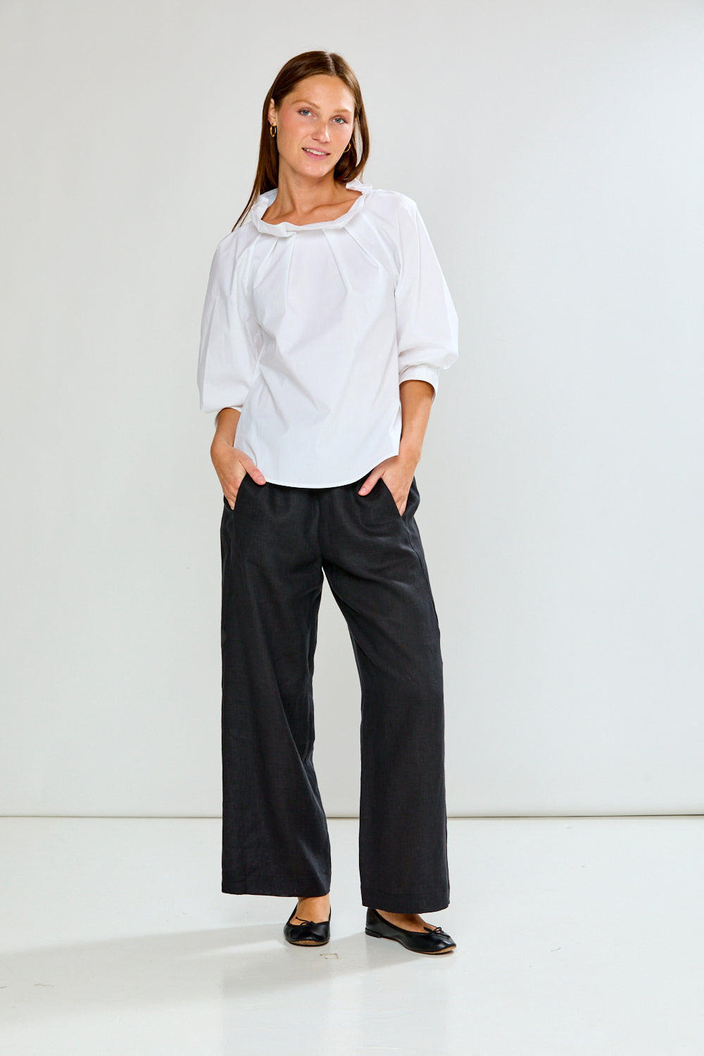 Woman wearing a white blouse and black pants against a white background