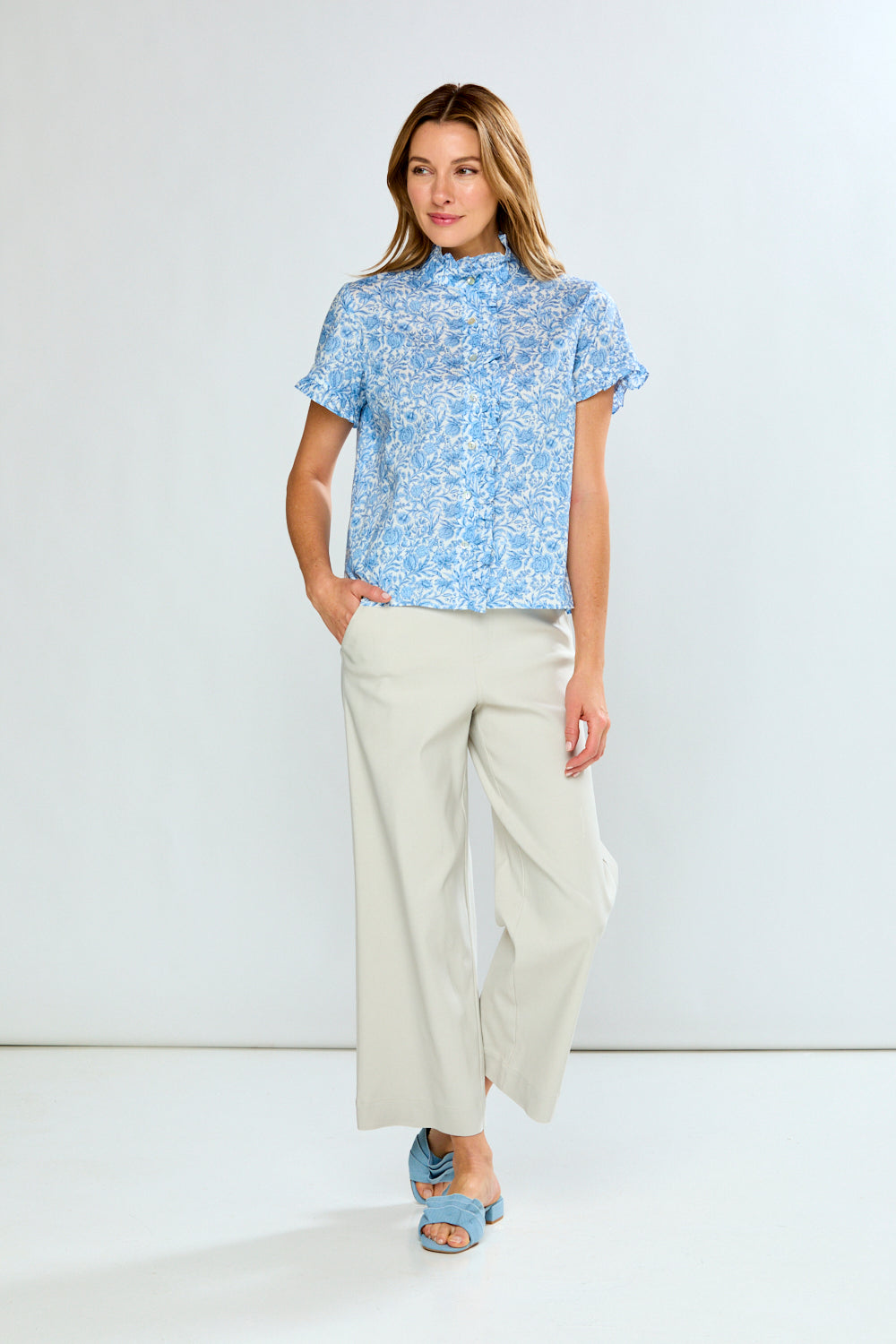 Woman wearing a blue patterned blouse and white pants on a white background