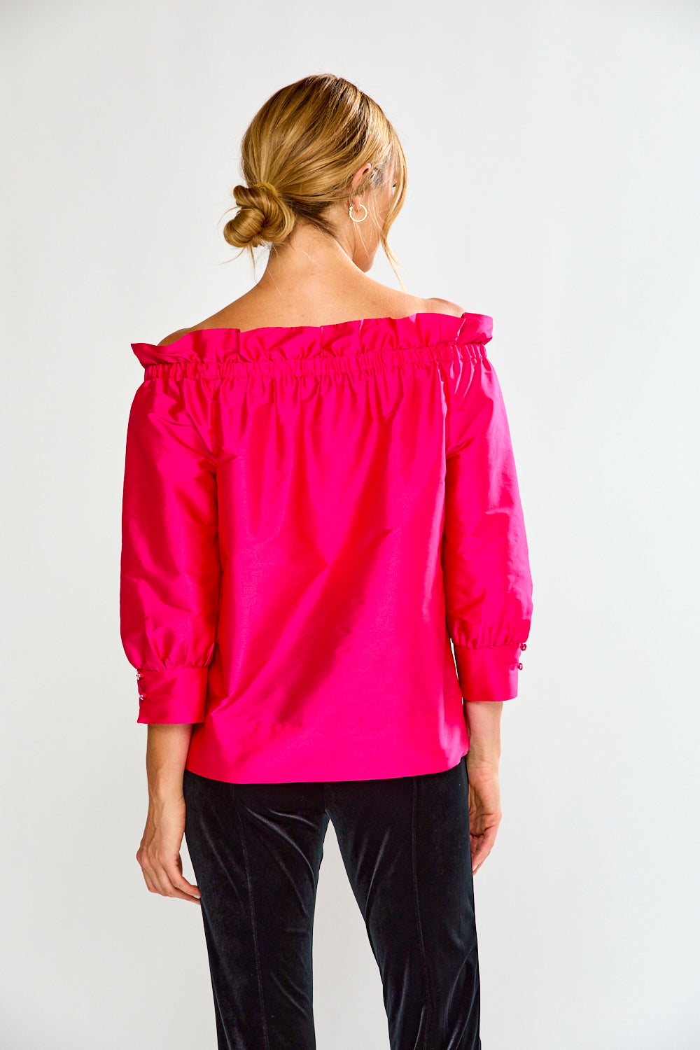 Woman wearing a bright pink off-shoulder top against a white background