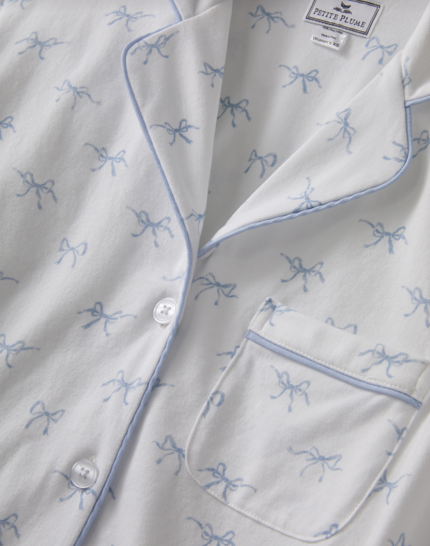 White shirt with blue bow patterns and button details, featuring a brand label.