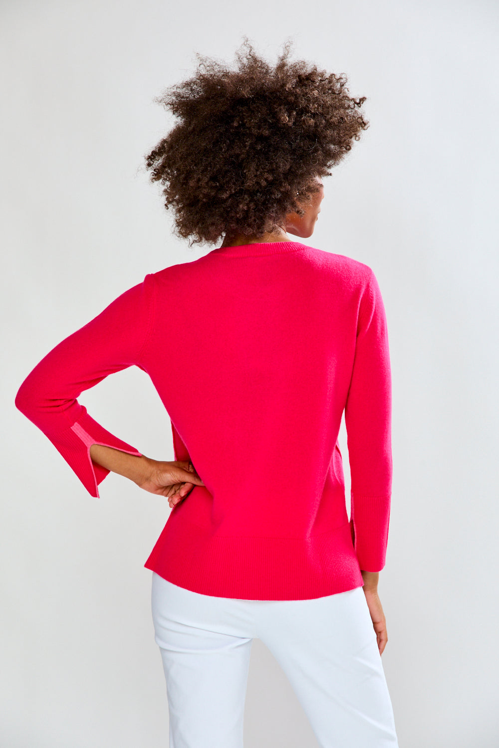 Person wearing a bright pink long-sleeve top and white pants on a plain background