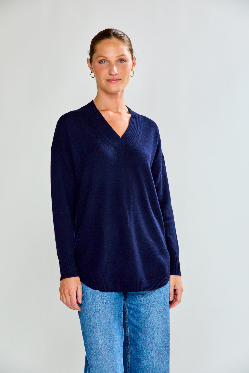 Woman wearing a navy sweater and blue jeans against a plain background
