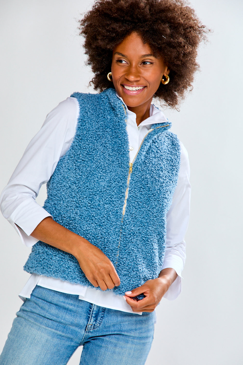 Woman wearing a blue textured vest over a white shirt and jeans on a white background