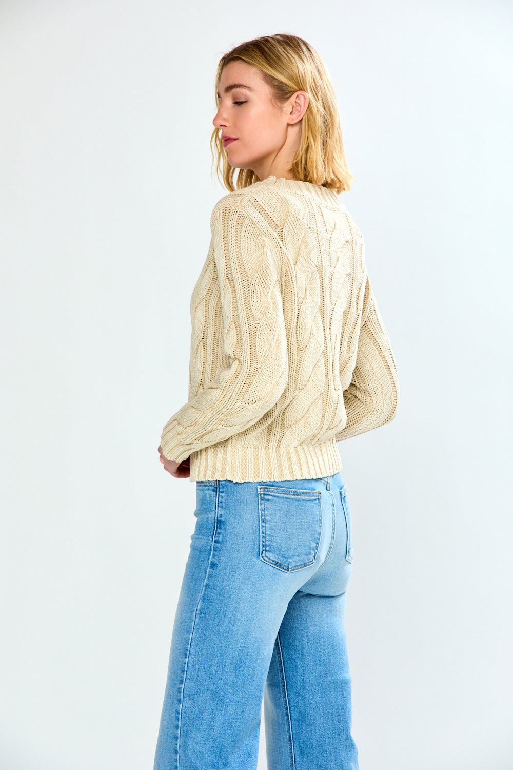 Woman wearing a pebble cable knit sweater and blue jeans on a white background