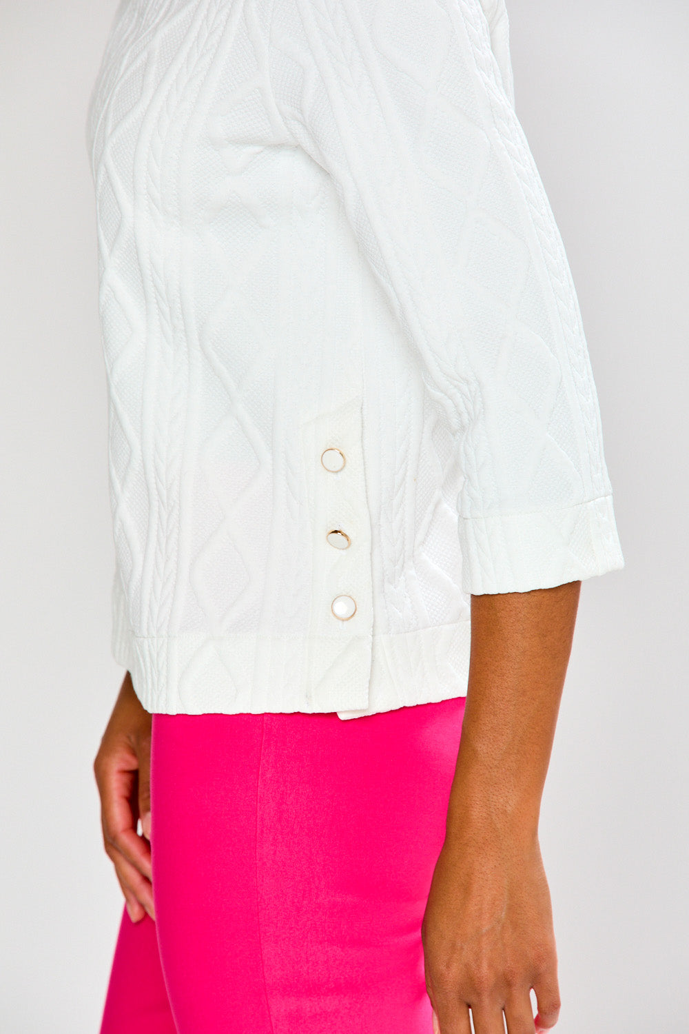 Woman wearing a white top and pink pants on a plain background
