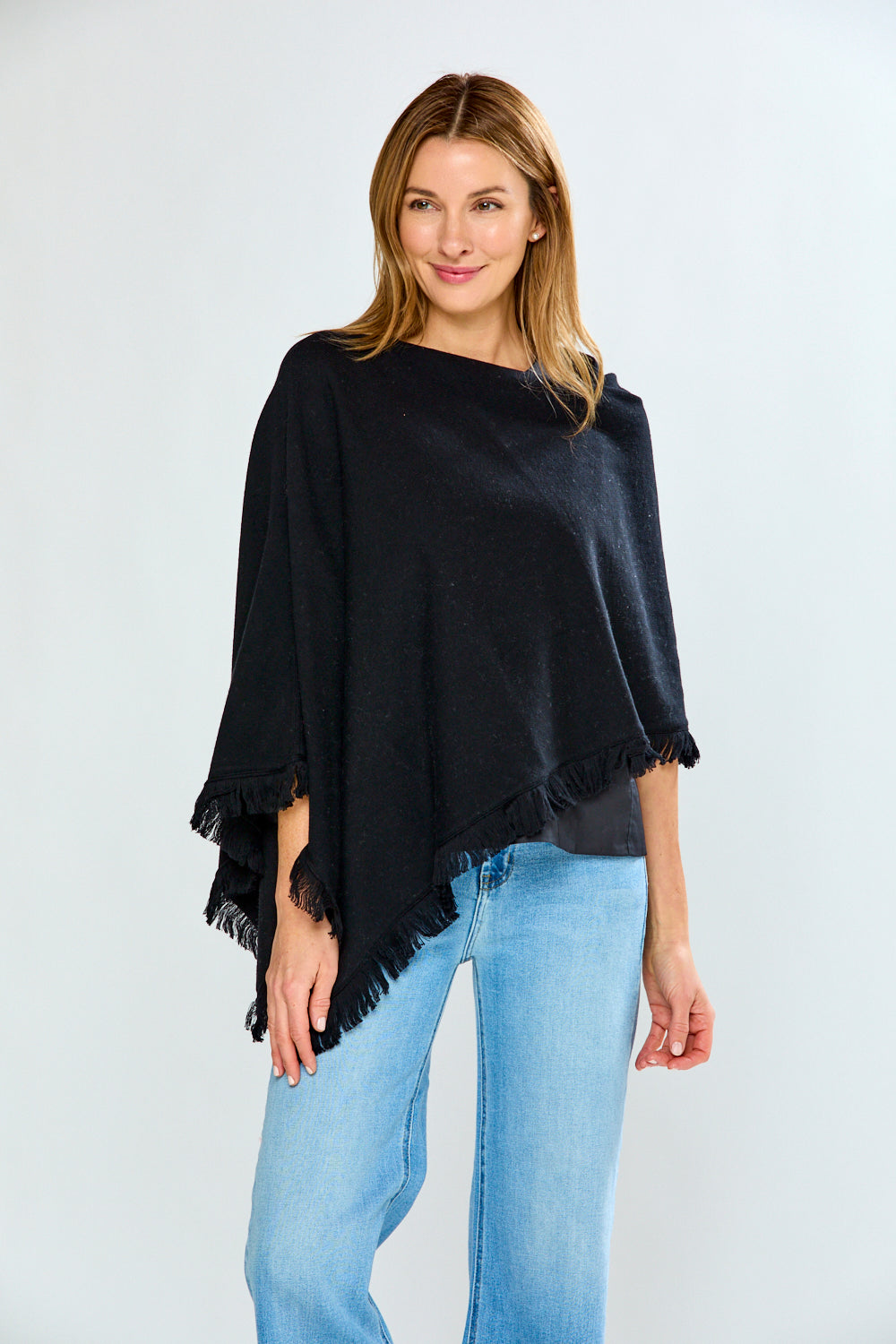 Woman wearing a black poncho and light blue jeans on a white background