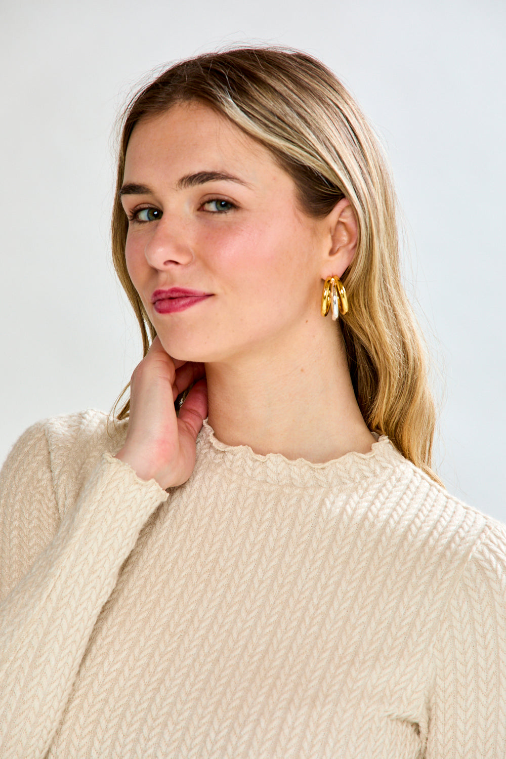 Woman wearing a beige ribbed shirt and brown pants against a white background