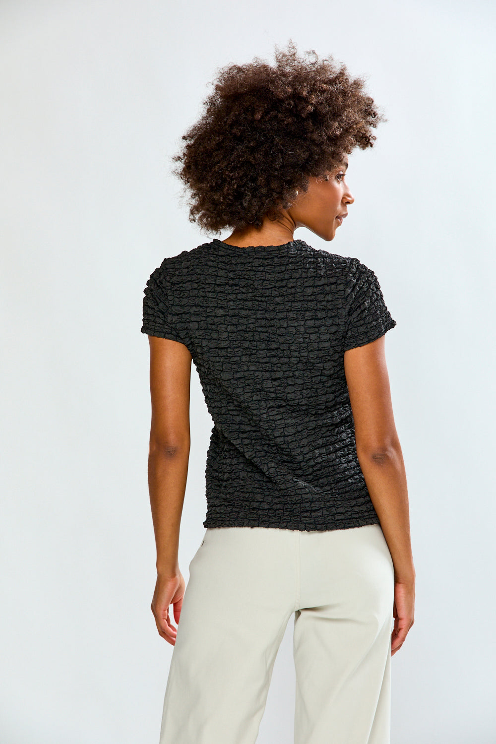 Person wearing a textured black top and white pants on a light gray background