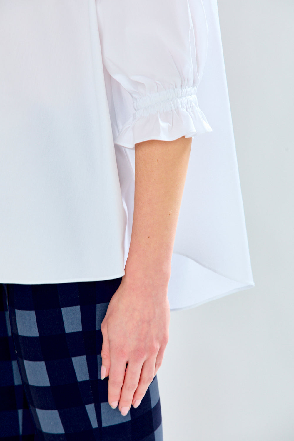 White blouse with rolled-up sleeves worn by a person, with a checkered pattern visible at the bottom.
