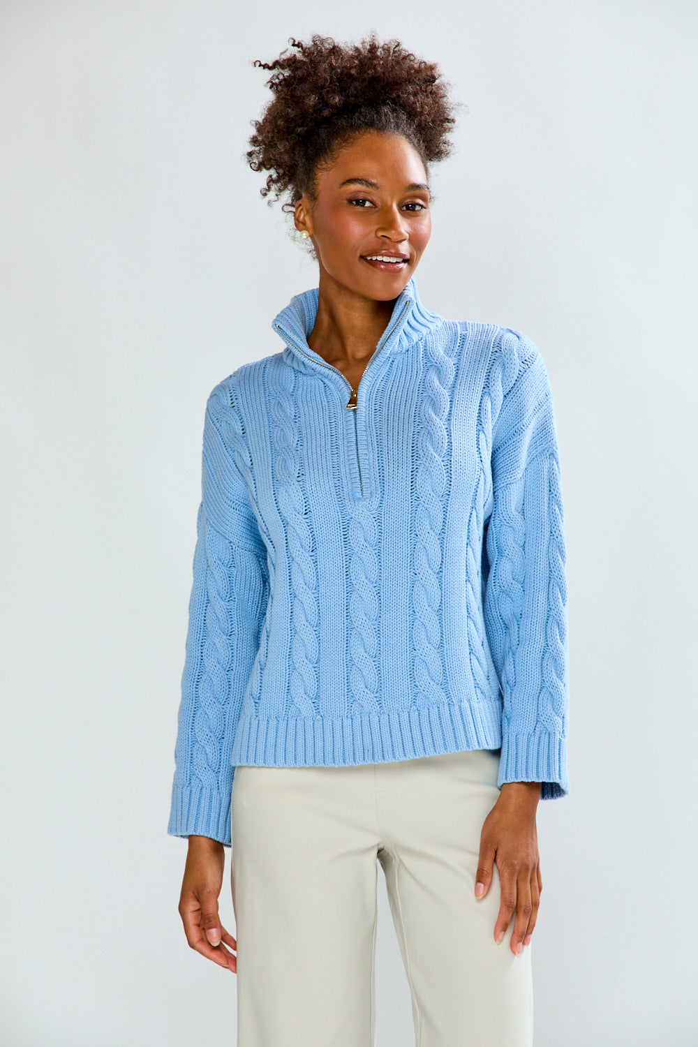 Woman wearing a light blue cable knit sweater against a plain background