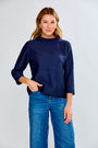 Woman wearing a navy blue textured sweater and blue jeans on a white background