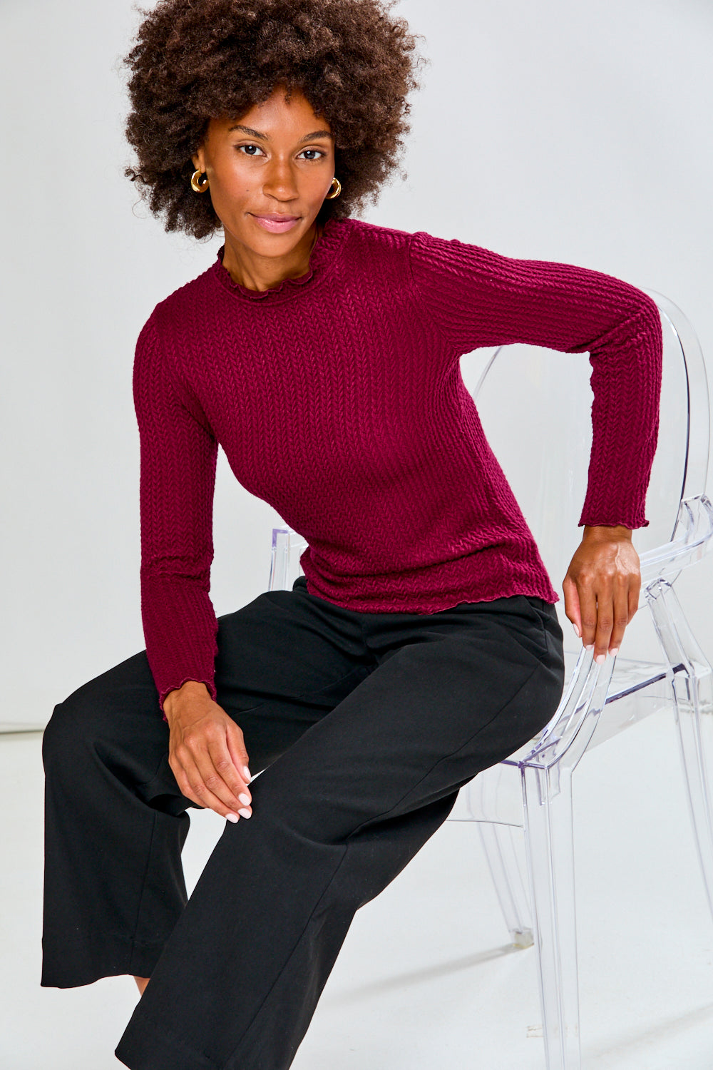 Woman wearing a burgundy shirt and black pants against a white background