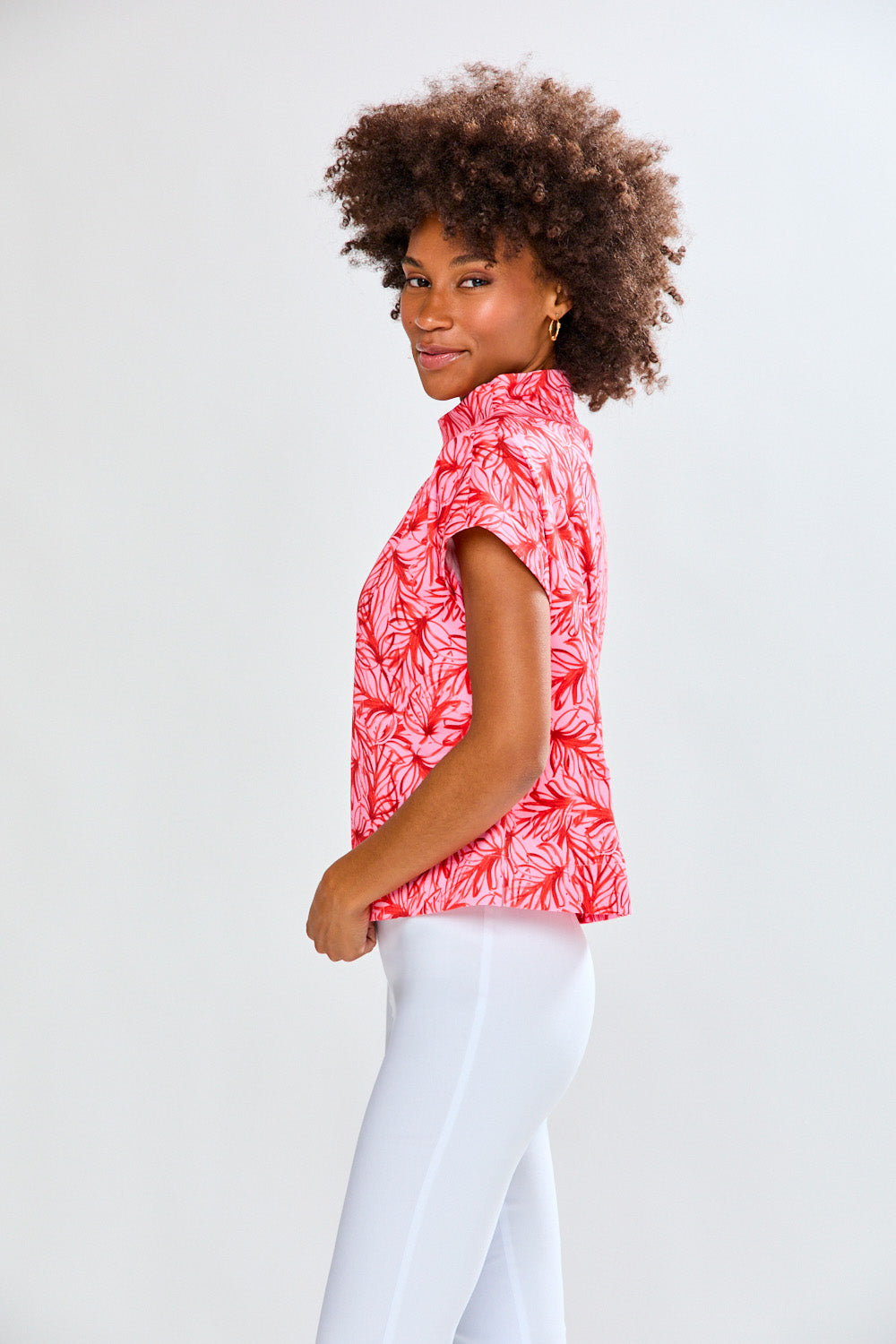 Woman wearing a red floral patterned shirt and white pants on a light gray background