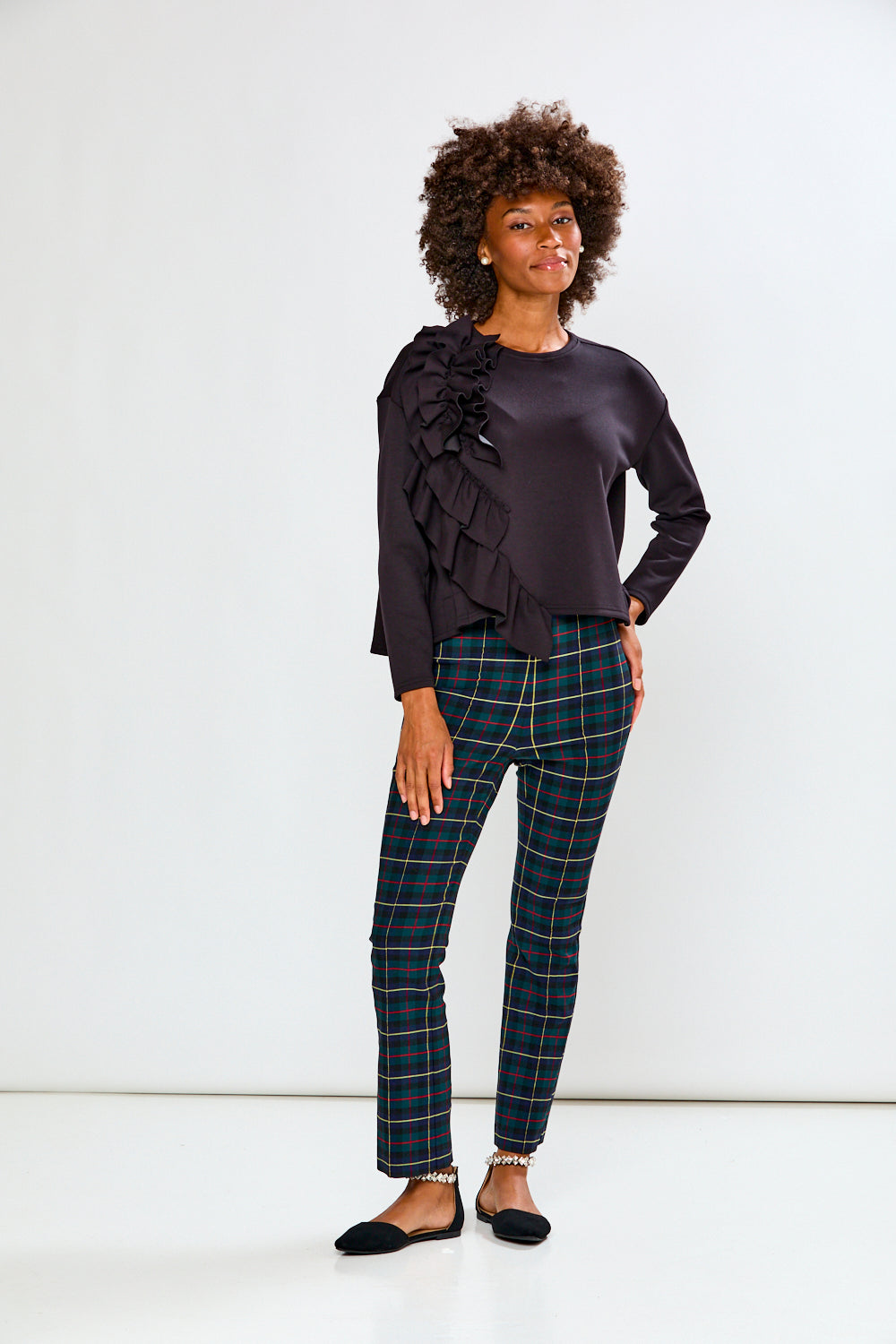 Woman wearing a black ruffled top and plaid pants against a white background