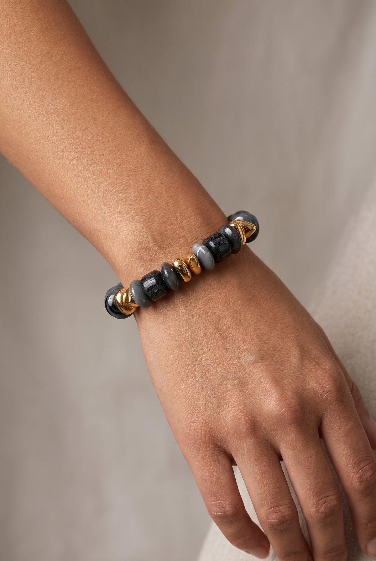 A close-up of a person's wrist wearing a beaded stretch bracelet with black, gray, and gold beads.