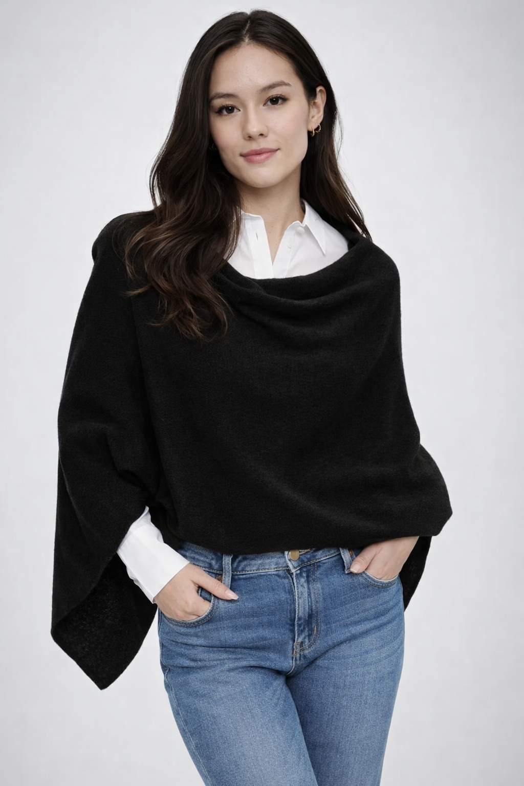 Woman wearing a black poncho over a white shirt and blue jeans on a white background
