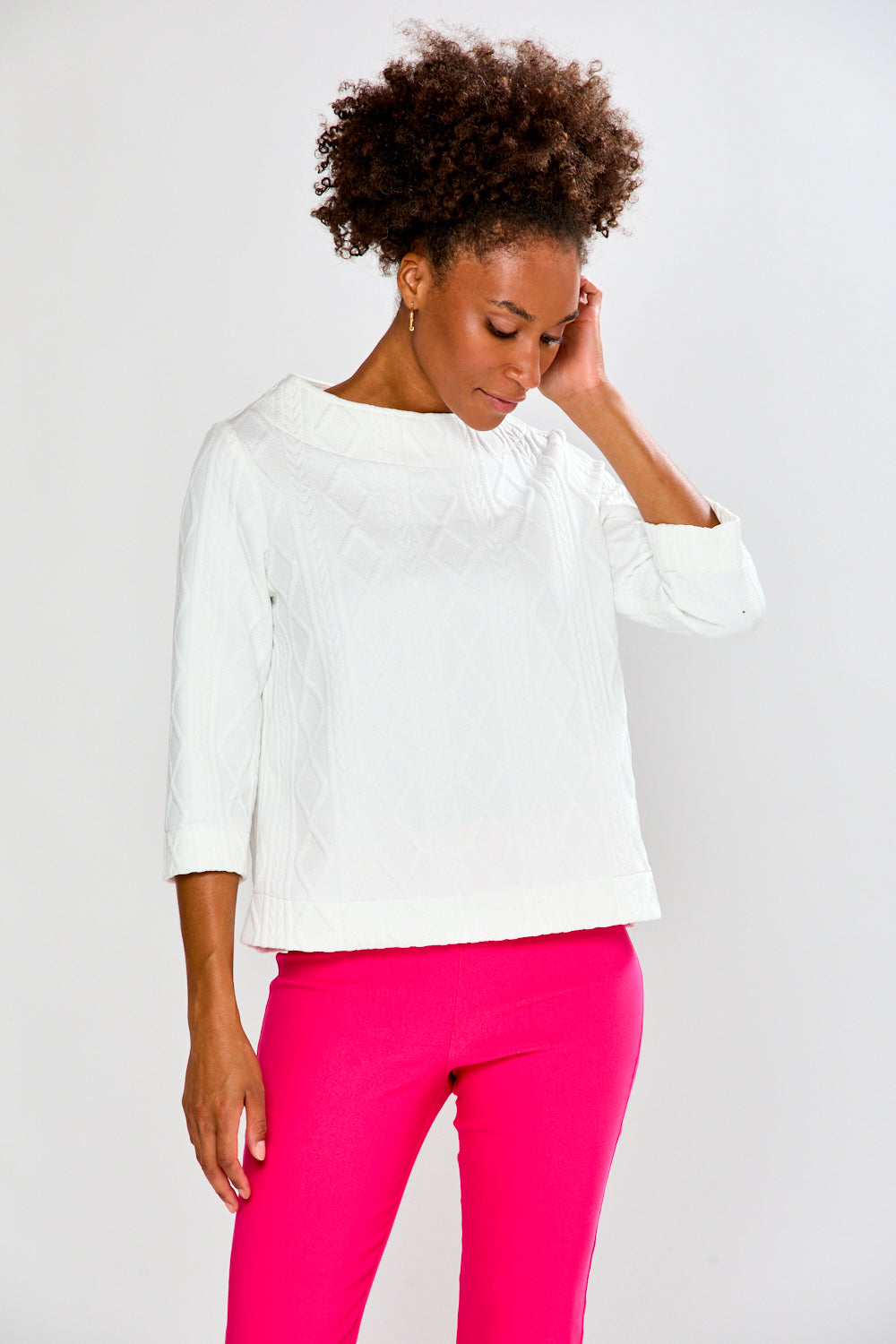 Woman wearing a white top and pink pants on a plain background