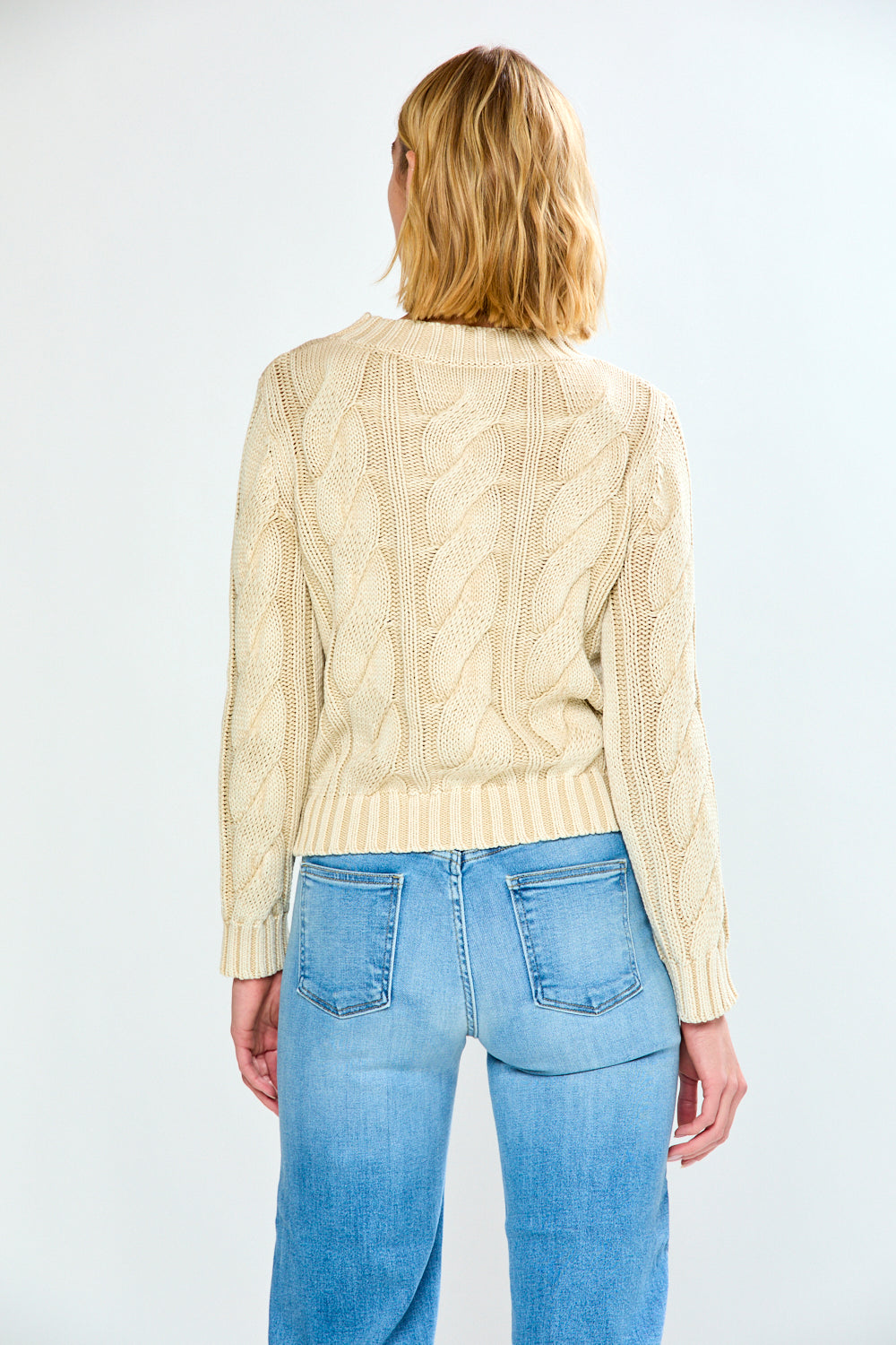 Woman wearing a pebble cable knit sweater and blue jeans on a white background