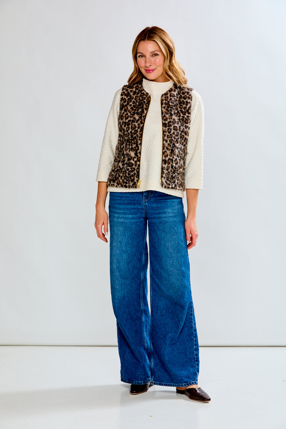 Woman wearing a leopard print vest, white shirt, and blue jeans on a white background