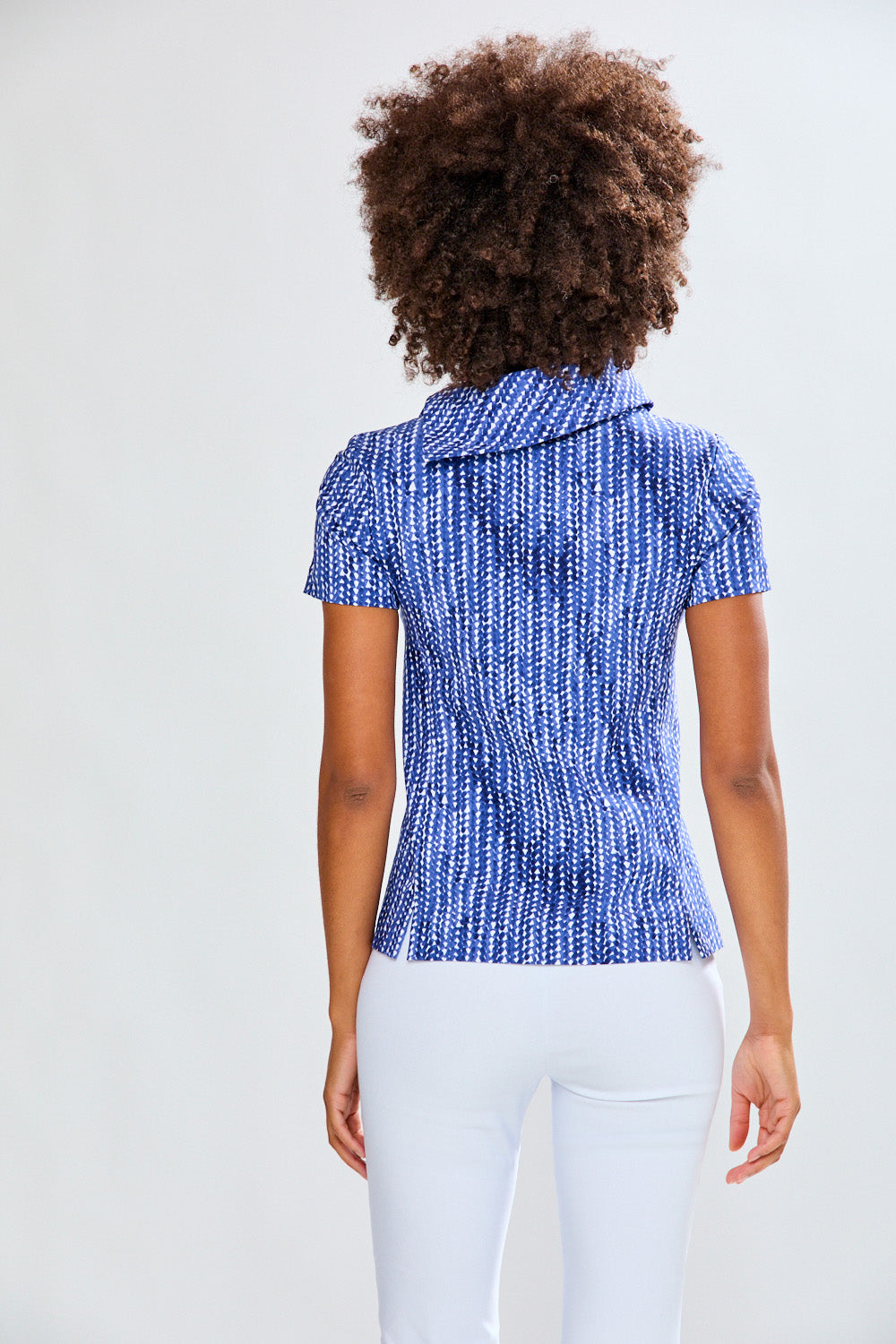 Woman wearing a blue patterned top and white pants against a plain background