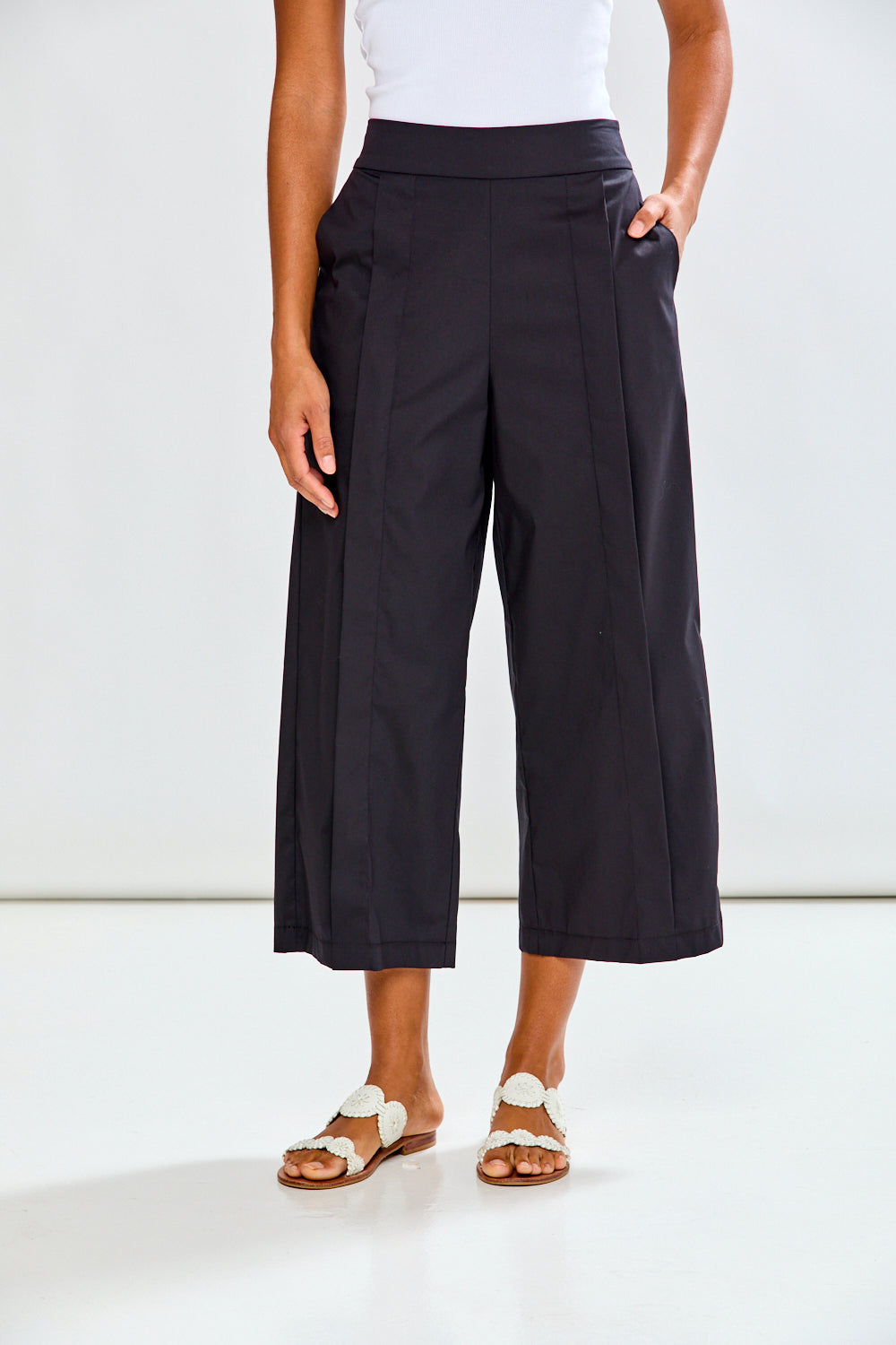 Woman wearing black wide-leg pants and white sandals on a white background