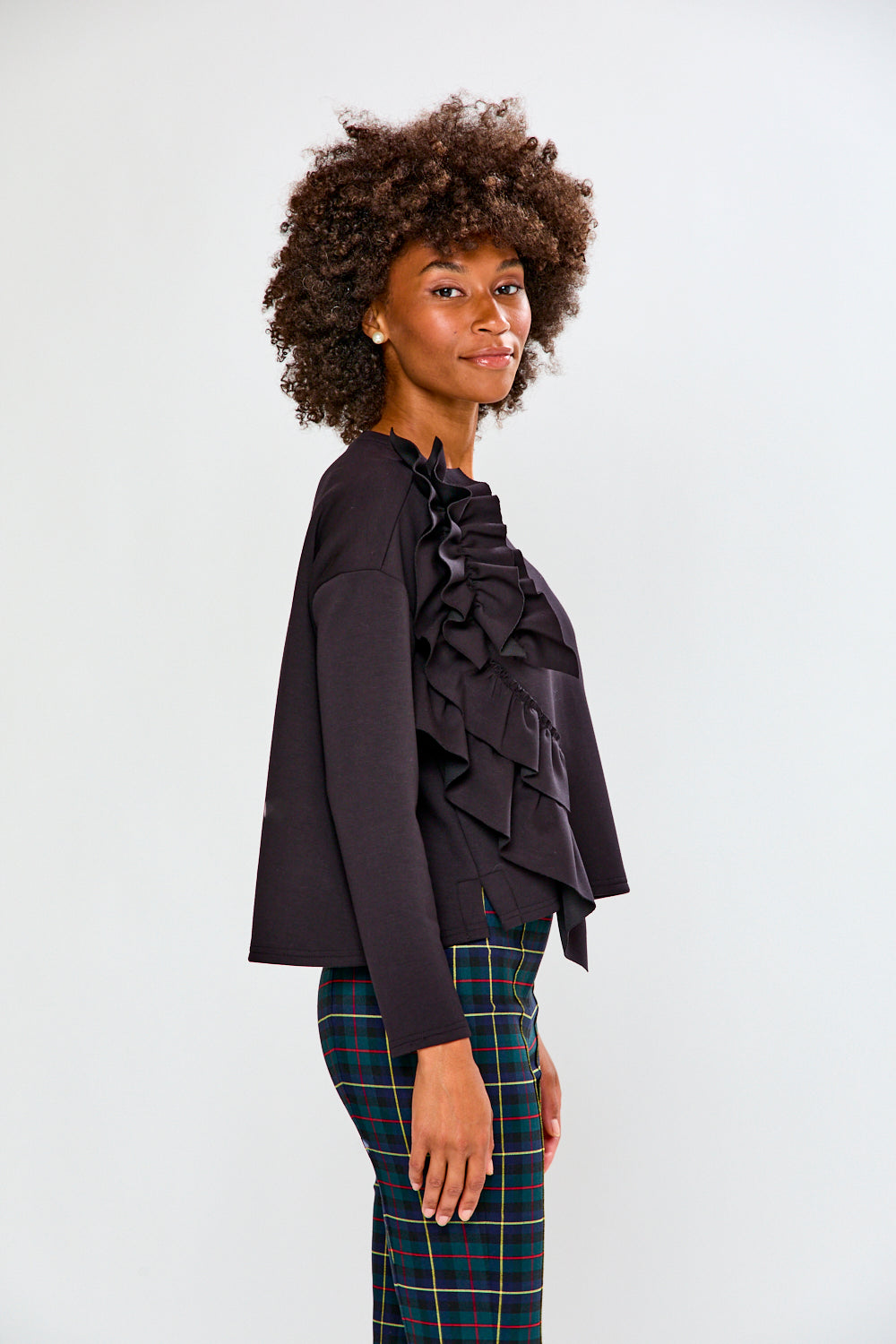 Woman wearing a black ruffled top and plaid pants on a white background