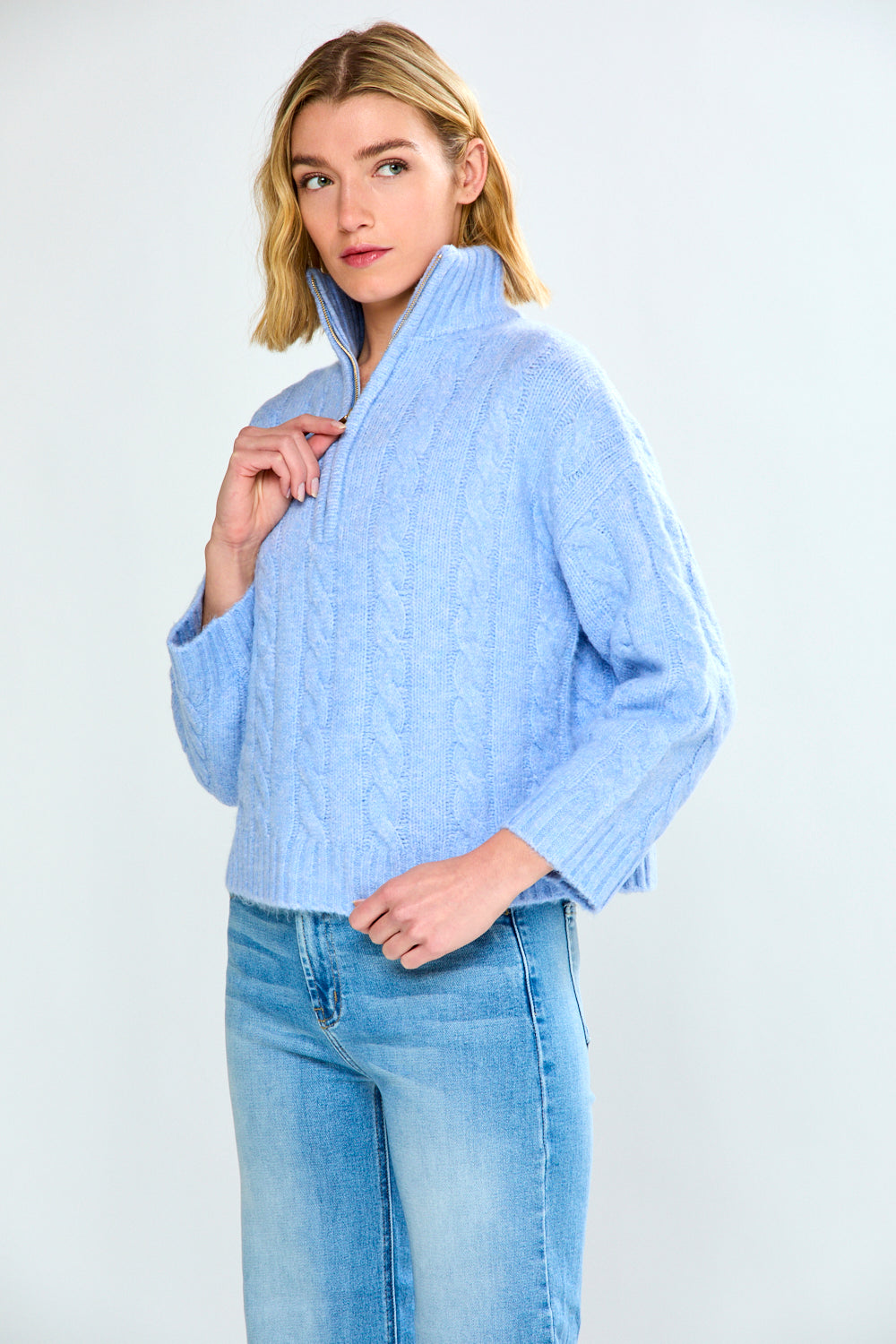Woman wearing a denim cable knit sweater and blue jeans on a white background