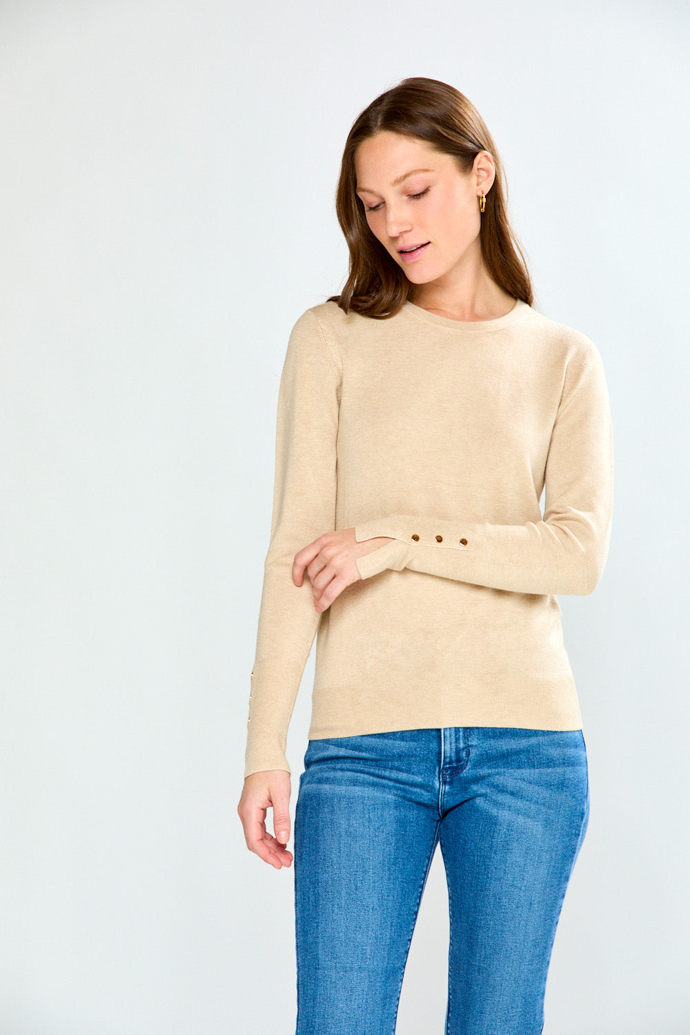 Woman wearing a sand sweater and blue jeans against a white background