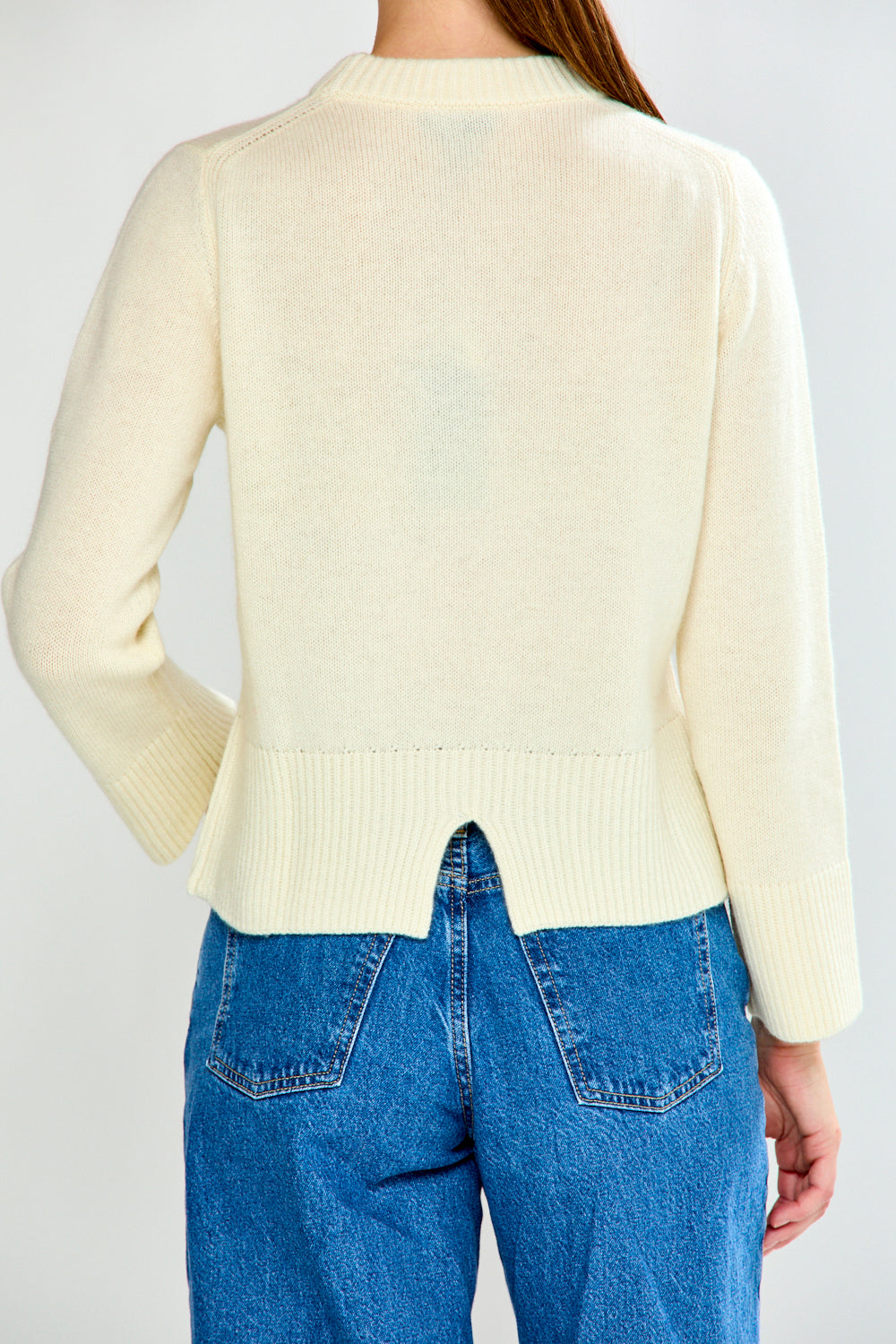 Woman wearing a cream sweater and blue jeans against a white background