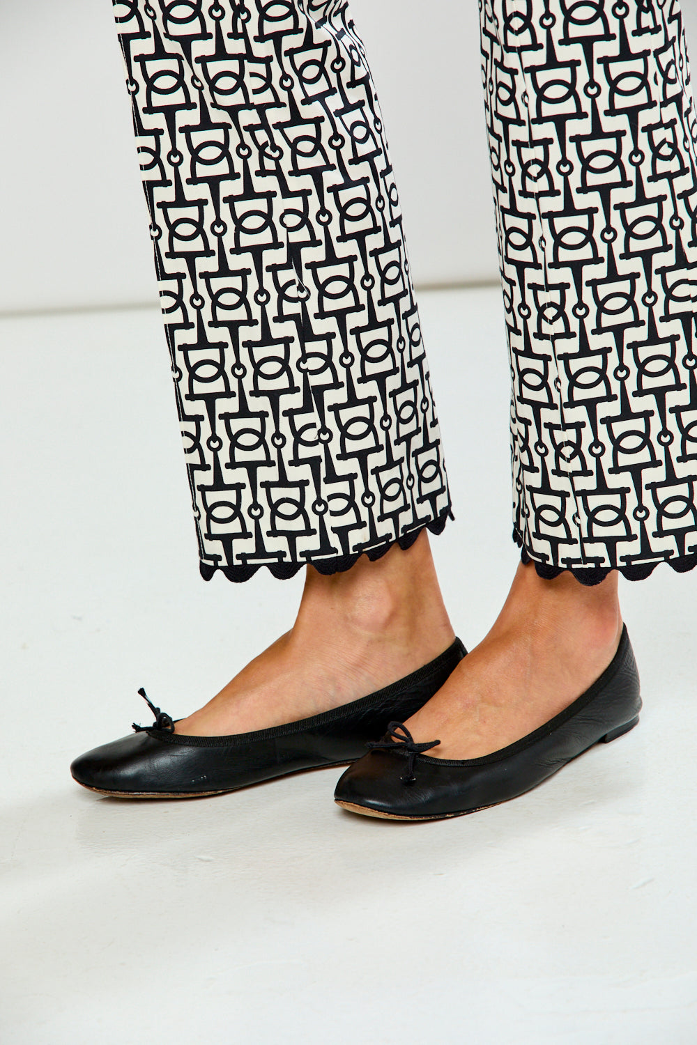 Black flats worn with patterned pants on a white background