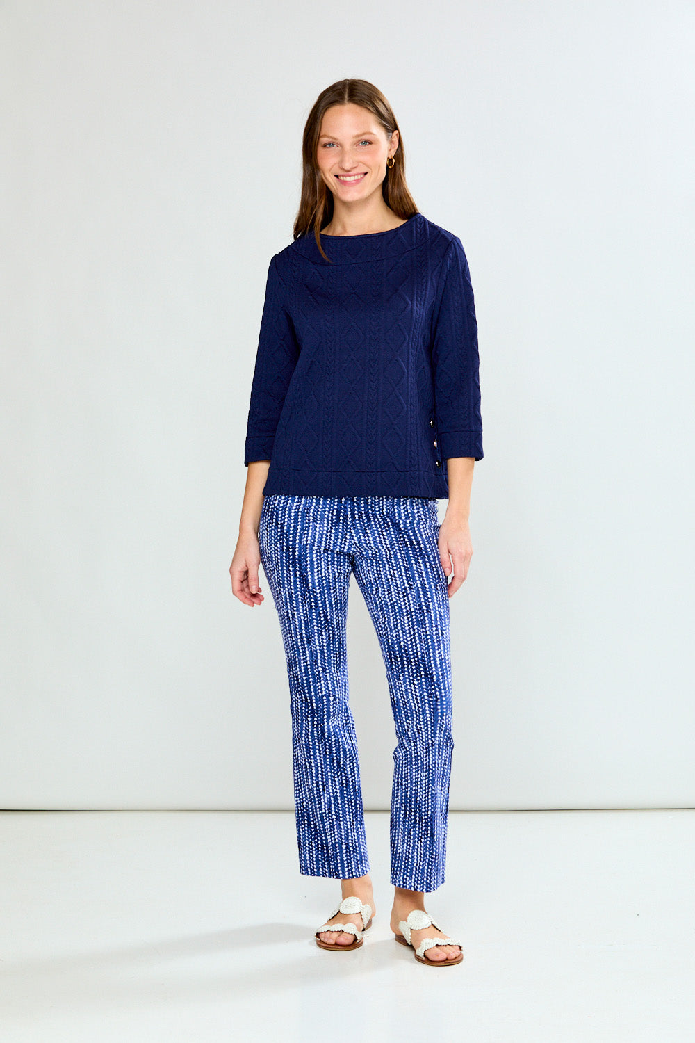 Woman wearing a navy blue cable knit top and patterned pants on a white background