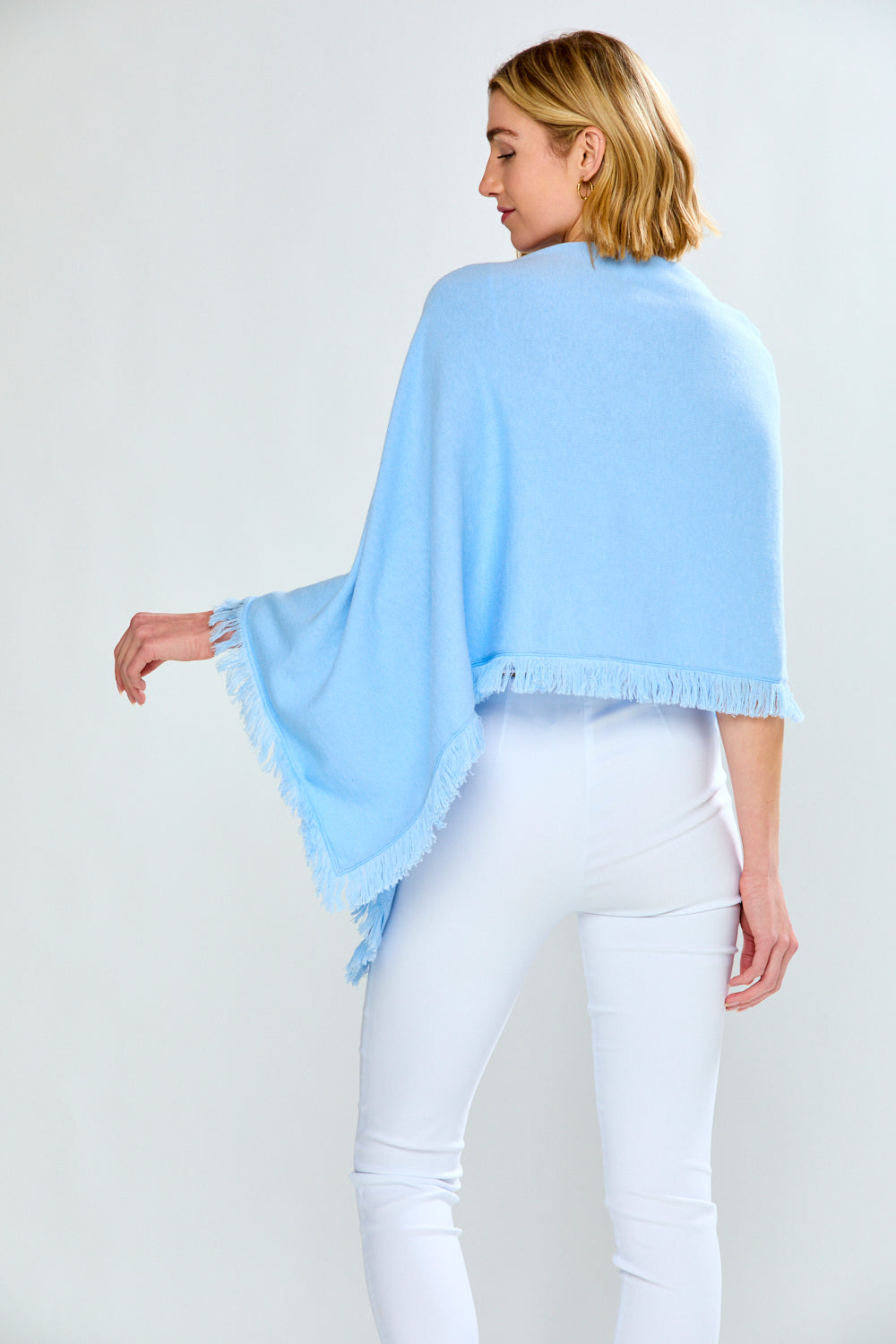 Woman wearing a light blue poncho over a white outfit on a plain background