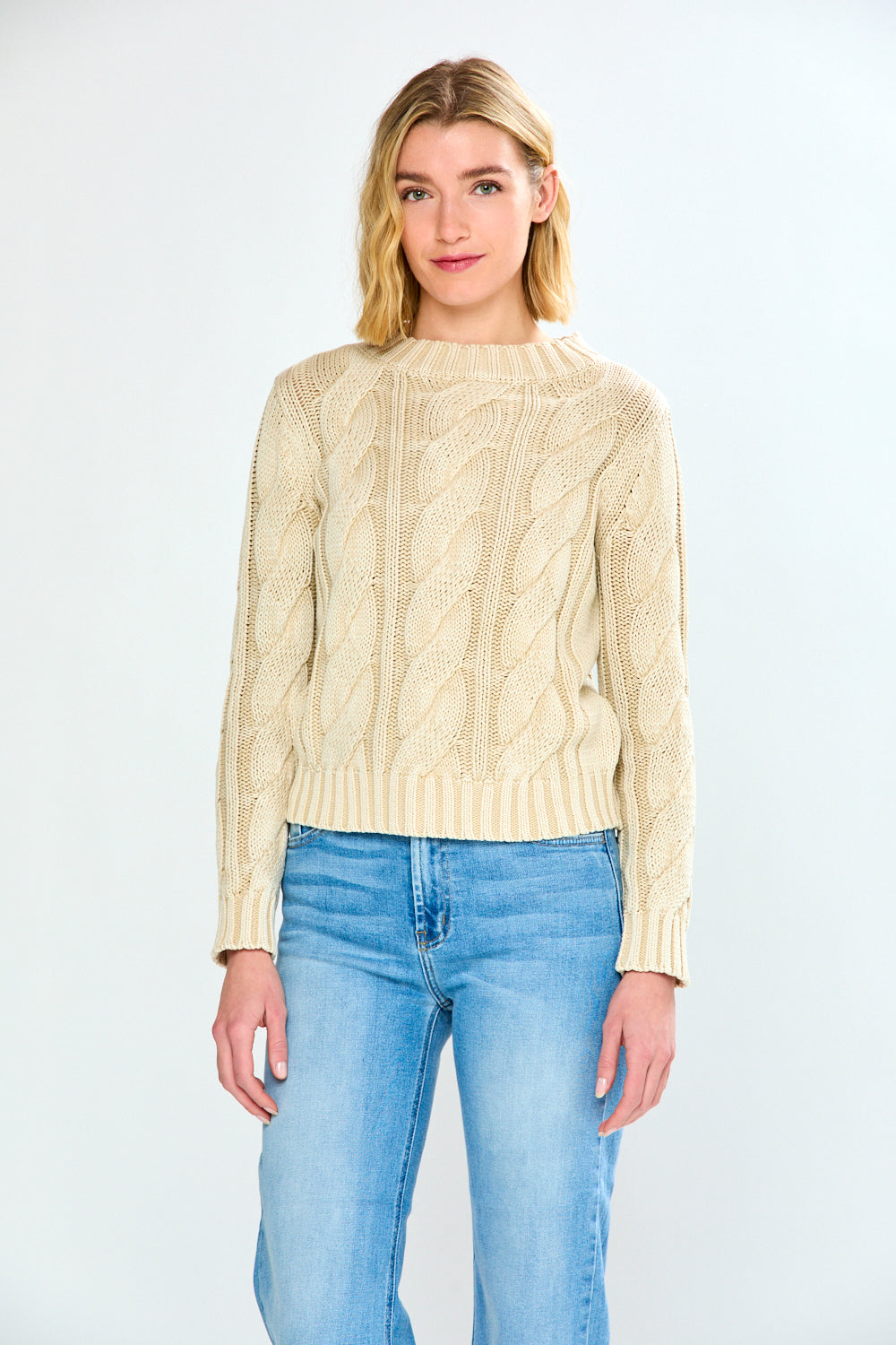Woman wearing a pebble cable knit sweater and blue jeans on a white background