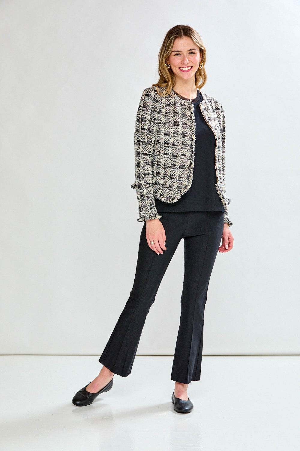 Woman wearing a black and white patterned jacket over a black top and pants on a white background